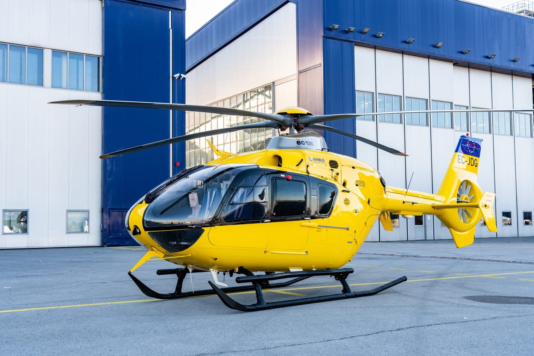 Yellow EC135 T2 helicopter in front of a hangar